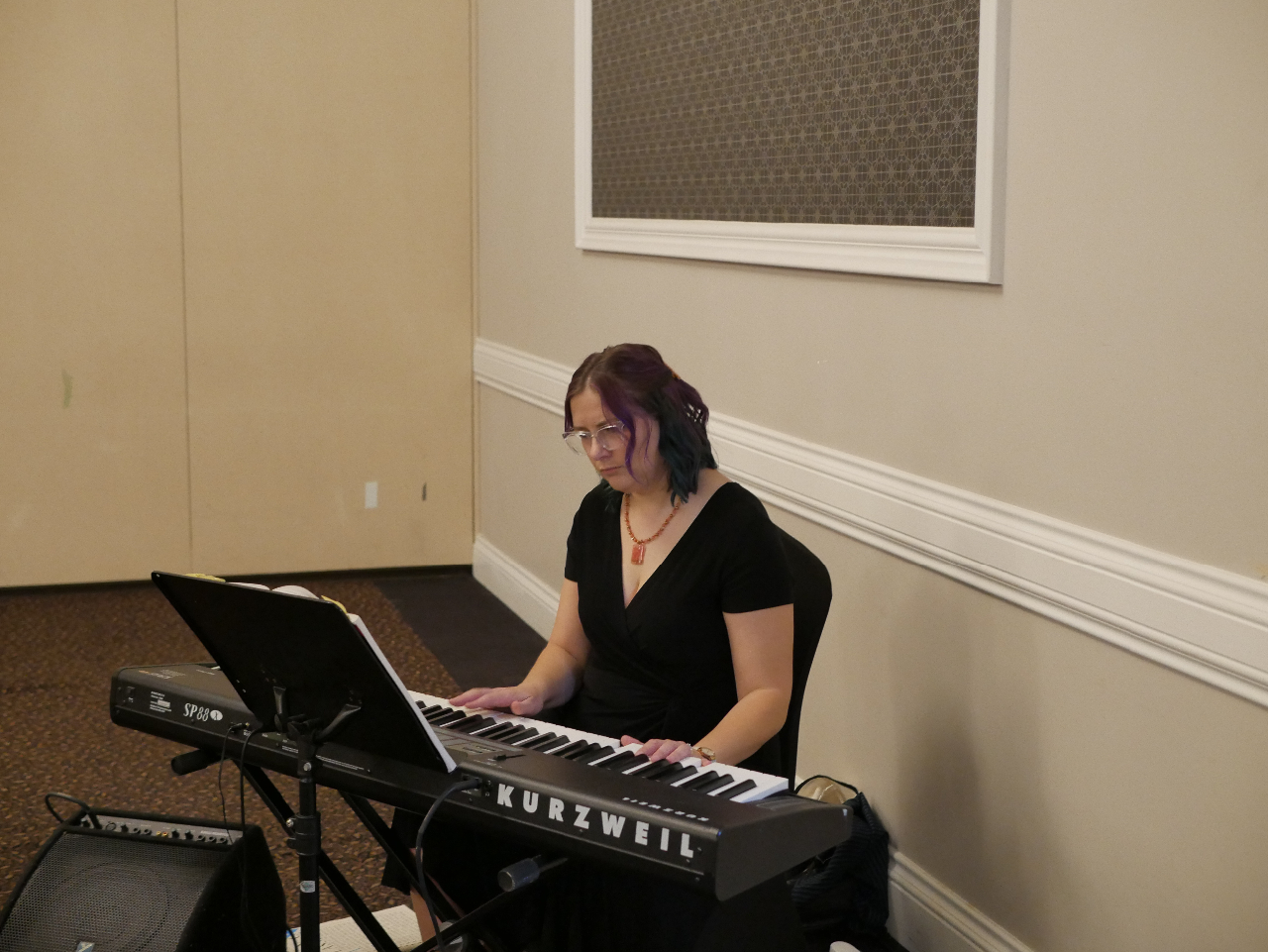 This photo features guest speaker Becky Verdun playing piano. She is seated and wearing a black dress.